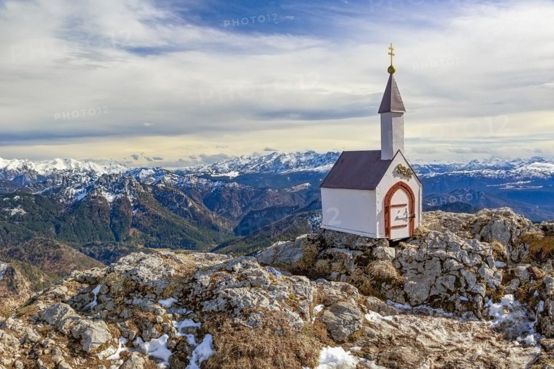 A lonely miniature chapel on the Hochgern summit in the Chiemgau mountains surrounded by rocks and snow in Bavaria Germany Europe