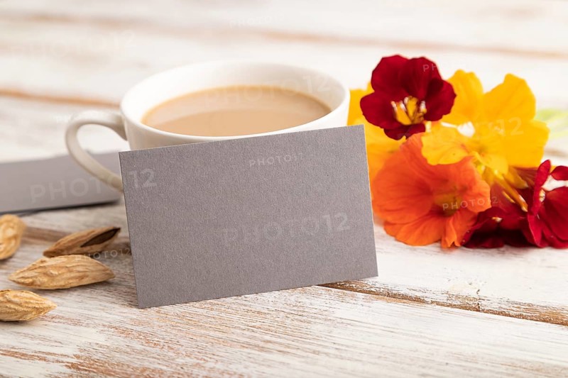 Gray paper business card mockup with orange nasturtium flower and cup of coffee on white wooden background. Blank, side view, copy space, still life. spring concept