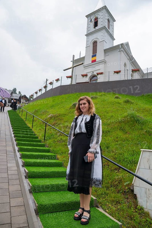 Young woman in folk traditional costume in front of a church on a green hill, woman in traditional costume, Vadu Motilor, Alba, Transylvania, Romania, Europe