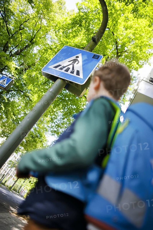 Symbol photo on the subject of schoolchildren in road traffic A six-year-old boy stands with his school bag on his back in front of a pedestrian crossing sign in front of a primary school. Berlin, 08.05.2024