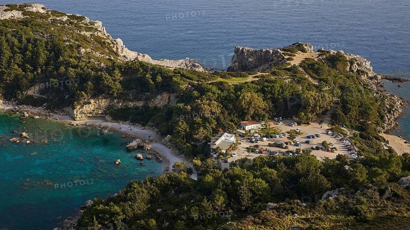 Car park and building in a rocky coastal landscape surrounded by trees and clear blue water, Anthony Quinn Bay, Vagies Bay, Rhodes, Dodecanese, Greek Islands, Greece, Europe