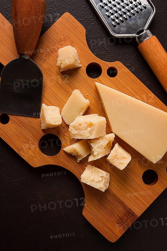 Hard cheese, parmesan, on a cutting board, cheese knife, grater, top view, no people