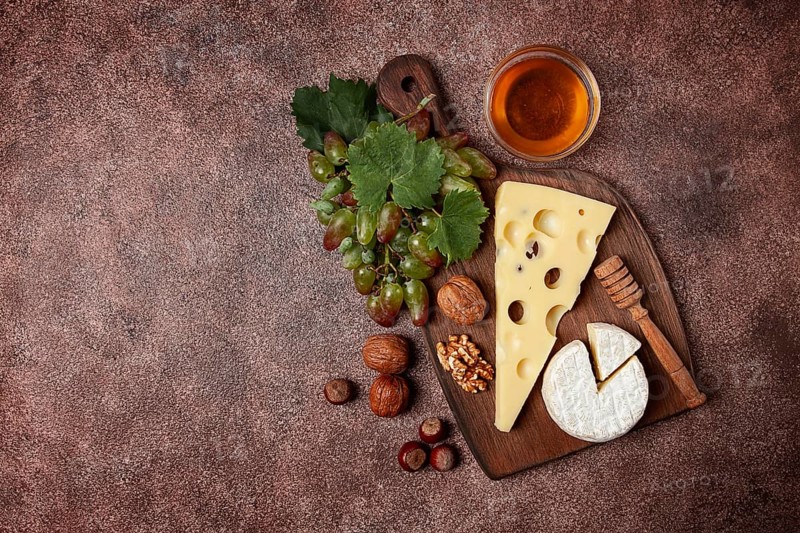Cheese with big holes, emmental, maasdam, brie cheese, on a cutting board, with grapes and honey, nuts, appetizer to wine, top view