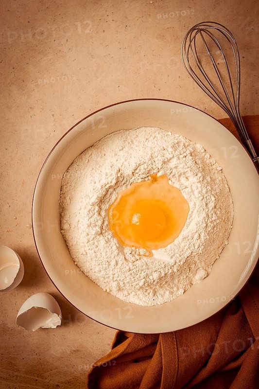 Food background, concept, plate with wheat flour, broken egg, whisk, kitchen towel, on a beige table, top view, rustic
