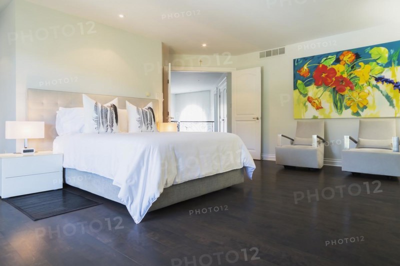 Master bedroom with queen size bed, white lacquered nightstands, upholstered armchairs and dark wooden flooring on upstairs floor inside a luxurious residential home, Quebec, Canada, North America