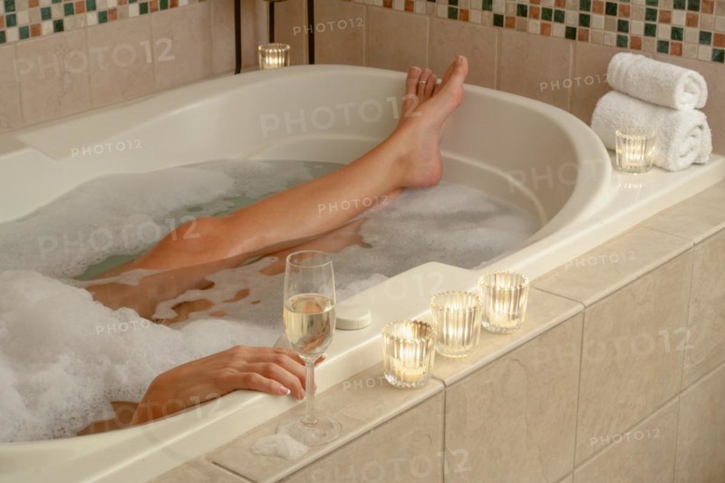 Woman relaxing in the bathroom spa tub with a glass of sparkling champagne and candles