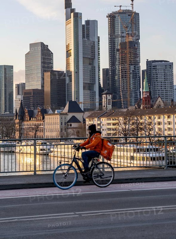 Skyline of the city centre of Frankfurt am Main, cyclist on the Alte Brücke, delivery service Lieferando, dusk, river Main, winter, Hesse, Germany, Europe