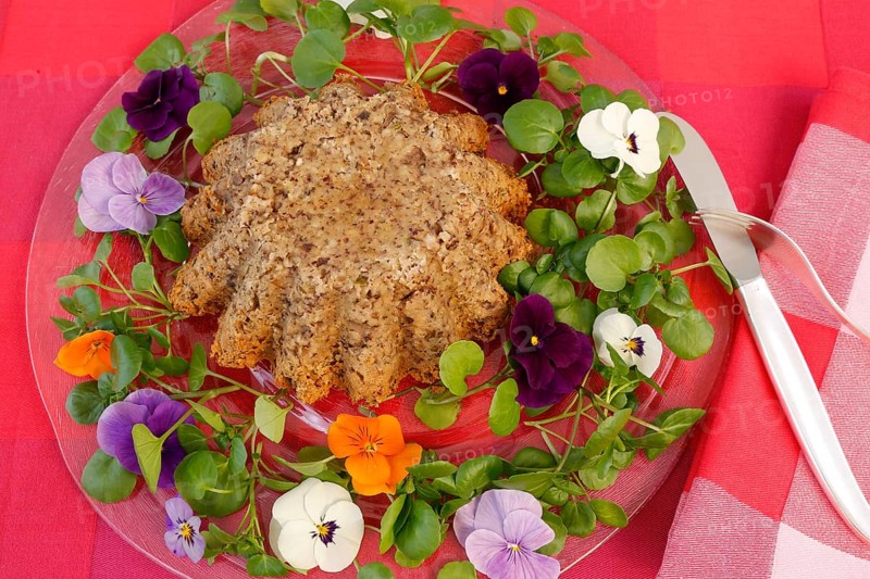 Vegetarian cuisine, chestnut roast, chestnut cake, chestnut roast, chestnut cake with hazelnuts, chestnut cake, savoury, vegan, salty, baked, from the oven, healthy, main course, glass plate, new kitchen, decoration with pansies, violet (Viola), cutlery, knife, fork, food photography, studio, Germany, Europe