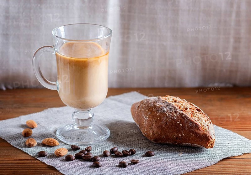 Glass cup of coffee with cream and bun on a wooden background and linen textile. close up, copy space