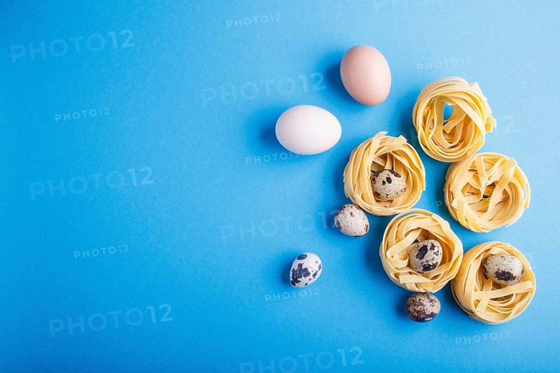 Raw uncooked tagliatelle pasta with quail eggs on a blue pastel background. top view. copy space. flat lay