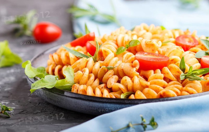 Fusilli pasta with tomato sauce, cherry tomatoes, lettuce and herbs on a black concrete background. side view, close up