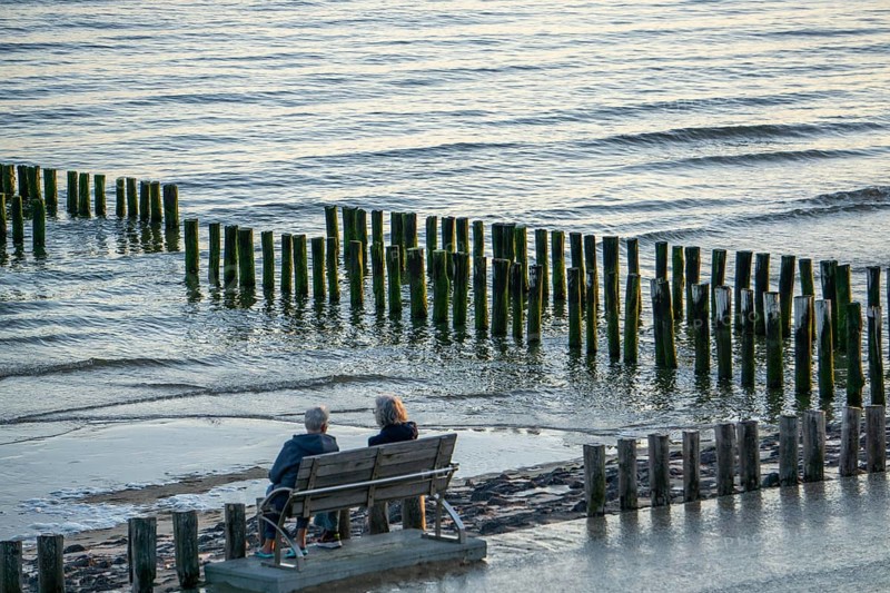 Two elderly woman on a bench on the beach, at high tide, breakwater, Netherlands