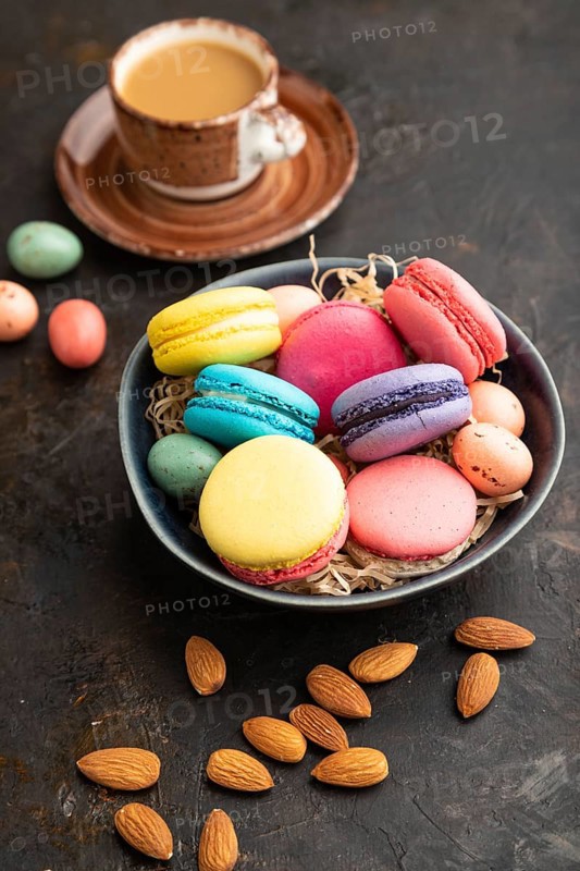 Multicolored macaroons and chocolate eggs in ceramic bowl, cup of coffee on black concrete background. side view, close up, still life. Breakfast, morning, concept