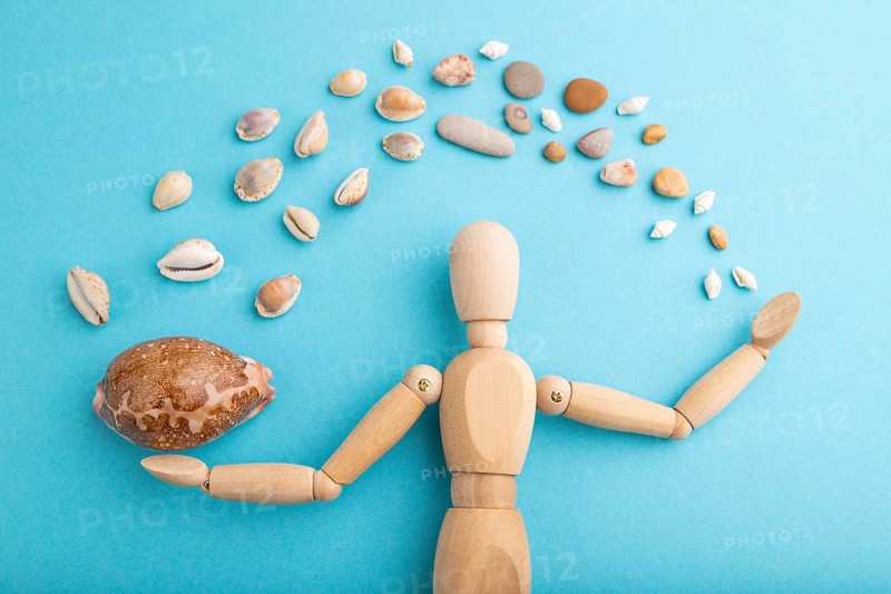 Wooden mannequin juggling sea shells on blue pastel background. close up, isolated, travel, vacation, summer concept