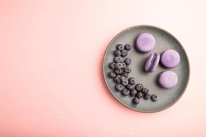 Purple macarons or macaroons cakes with blueberries on ceramic plate on a pastel pink background. Top view, flat lay, copy space