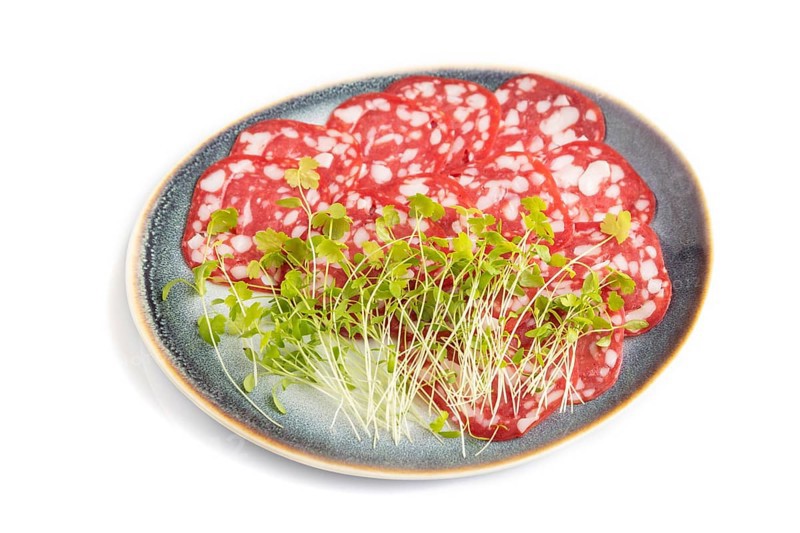 Slices of smoked cervelat salami sausage with spinach microgreen isolated on white background. Side view, close up