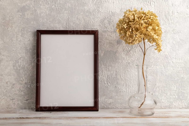 Brown wooden frame mockup with dried hydrangea in glass on gray concrete background. Blank, vertical orientation, still life, copy space