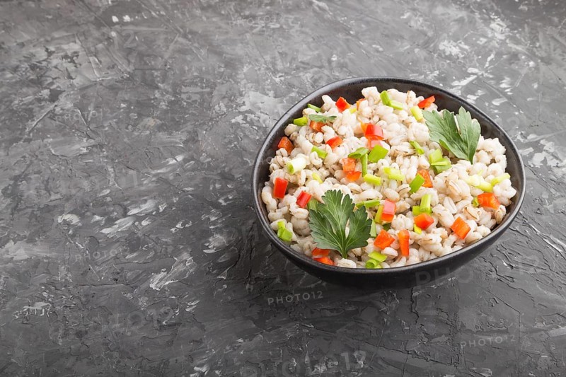 Pearl barley porridge with vegetables in blue ceramic bowl on a black concrete background. side view, copy space. Russian traditional cuisine