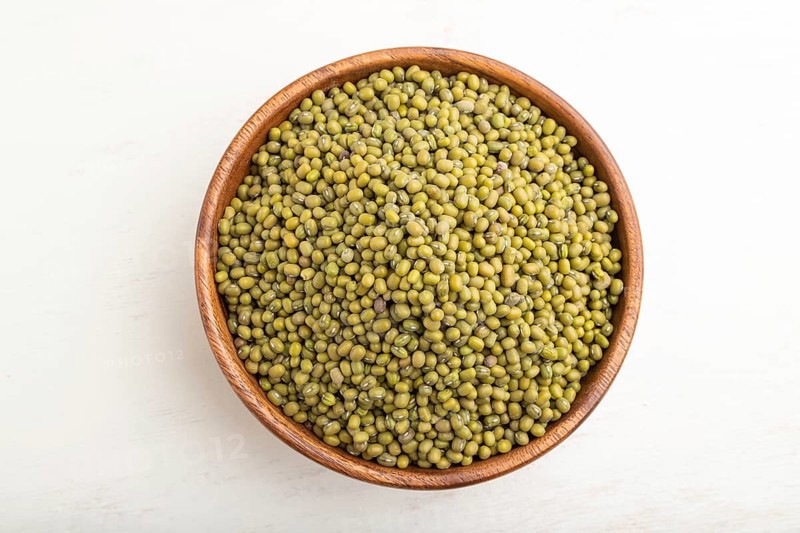Wooden bowl with raw green mung bean on a white wooden background. Top view, flat lay, close up