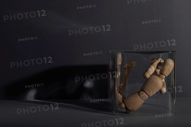 Wooden mannequin locked in a glass cube on gray background. captivity, break rules, loneliness, depression disorder concept. copy space