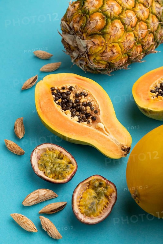 Ripe cut papaya, pineapple, melon, passion fruit, almonds on blue pastel background. Side view, close up. Tropical, healthy food, vacation, holidays concept