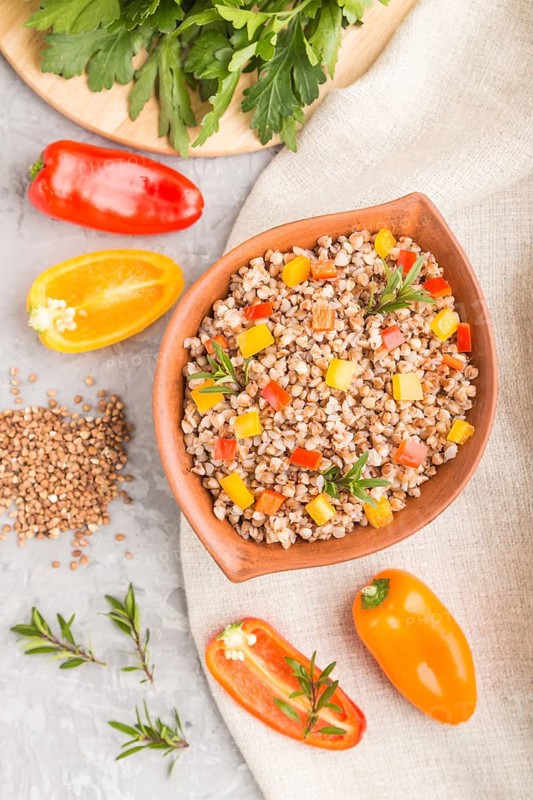 Buckwheat porridge with vegetables in clay bowl on a gray concrete background and linen textile. Top view, flat lay, close up. Russian traditional cuisine