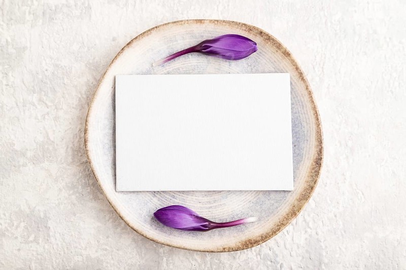 White paper invitation card, mockup with crocus flowers on ceramic plate and gray concrete background. Blank, flat lay, top view, still life, copy space, wedding invitation