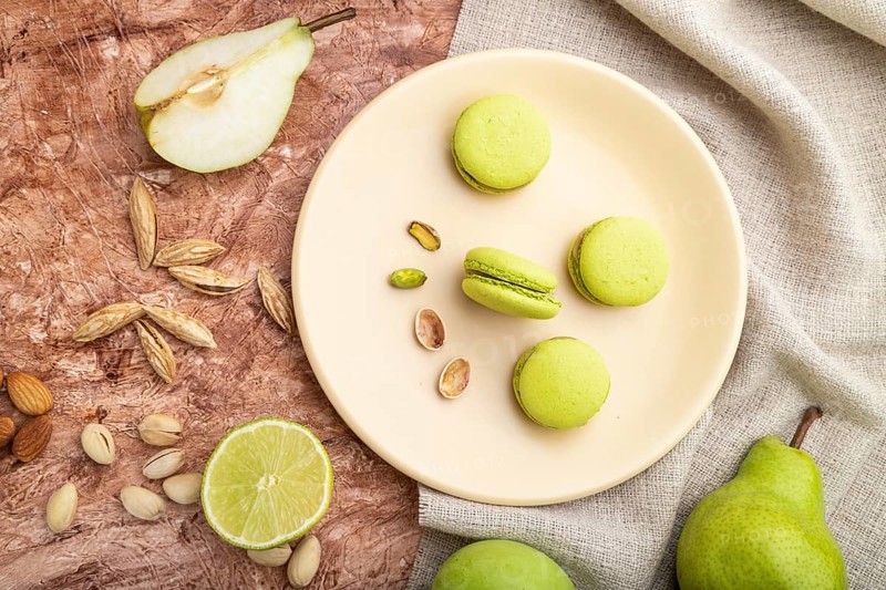 Green macarons or macaroons cakes with cup of coffee on a brown concrete background and linen textile. Top view, flat lay, close up