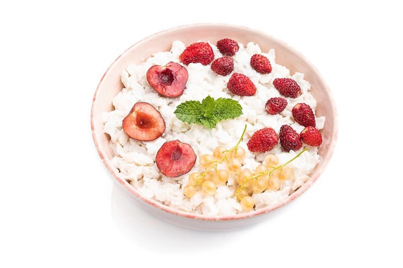 Rice flakes porridge with milk and strawberry in ceramic bowl isolated on white background. Side view, close up