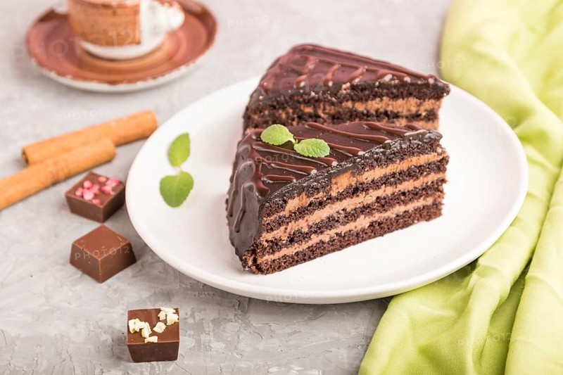 Homemade chocolate cake with milk cream and a cup of coffee on a gray concrete background with green textile. side view, close up, selective focus