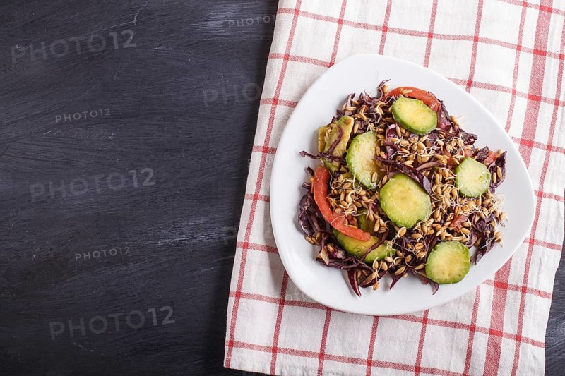Vegetarian salad of purple cabbage, germinated wheat, tomatoes and avocado on linen tablecloth, black background, top view, copy space