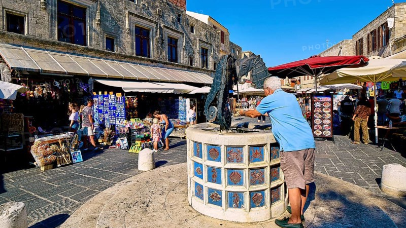 Martyrs Square, market square with seahorse fountain and shops in the background, sunny day with people in the picture, Rhodes Old Town, Rhodes Town, Rhodes, Dodecanese, Greek Islands, Greece, Europe