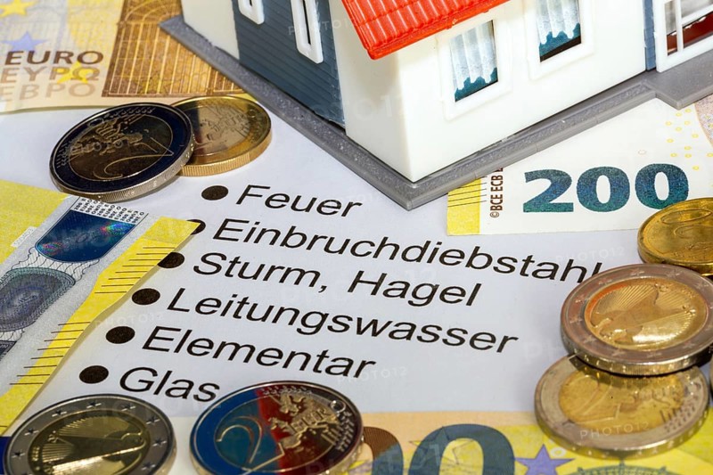 Symbolic image of building insurance: close-up of contract documents, a model house, euro banknotes and euro coins