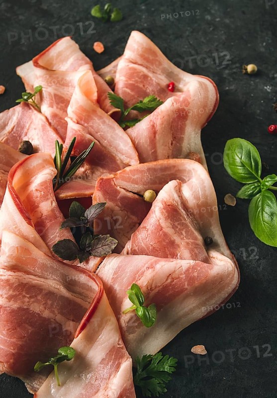Raw bacon, sliced, with micro greenery and spices, on a black background, close-up