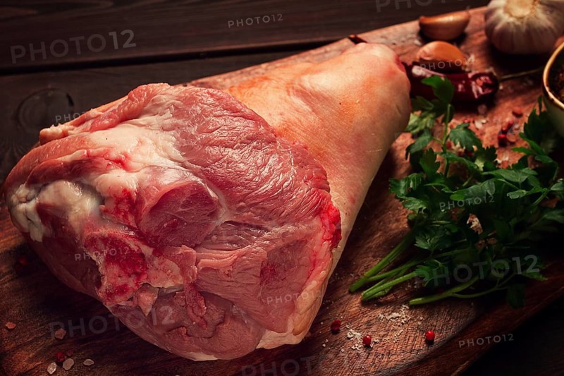 Raw pork knuckle, on a wooden chopping board, with spices, close-up, top view, no people