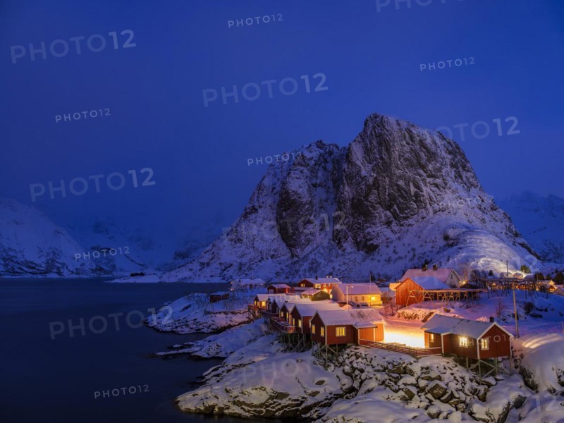 Rorbuer huts of Hamnoy at the fjord at dusk, snowy mountains in the background, Hamnøy, Reine, Moskenesøya, Lofoten, Norway, Europe