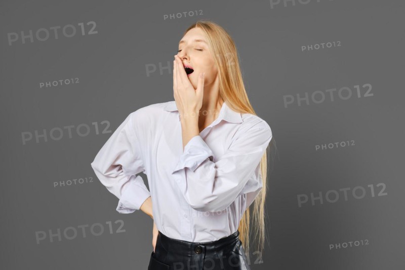 Young woman yawns covering her mouth with her hand