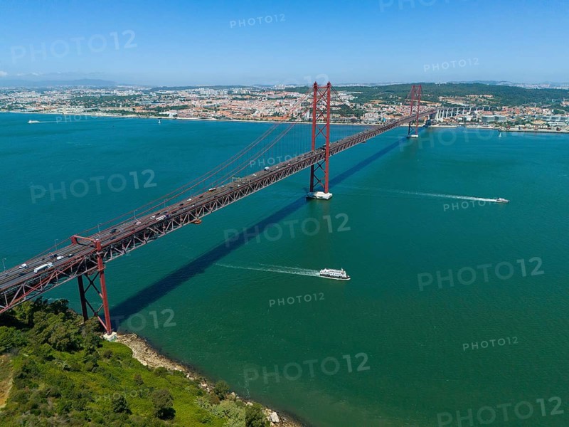 Red bridge spanning the water, lined with boats, with a city and nature in the background on a sunny day, aerial view, Ponte 25 de Abril, bridge of 25 April, suspension bridge over the Tagus, double deck bridge, road traffic and railway traffic, Lisbon, Lisboa, Portugal, Europe