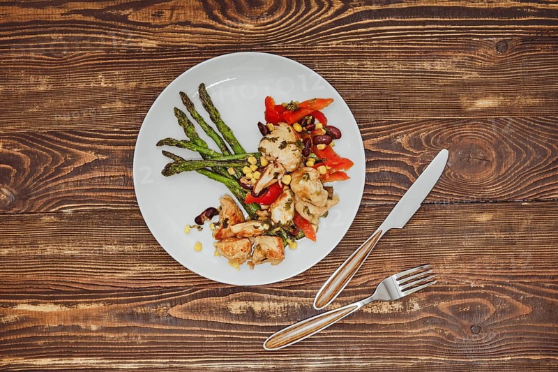 Overhead view of spicy chicken stew with vegetables and fried asparagus on wooden table