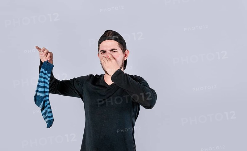 Man holding sock covering his nose isolated.Teeneger holding a stinky sock isolated. smelly socks concept
