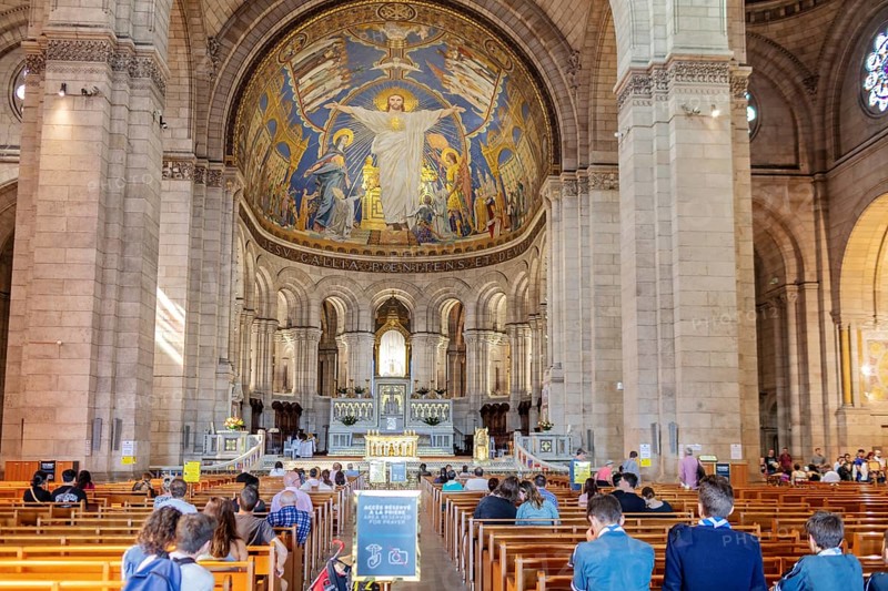 Church interior with a large mosaic of Jesus above the altar, people praying, Paris