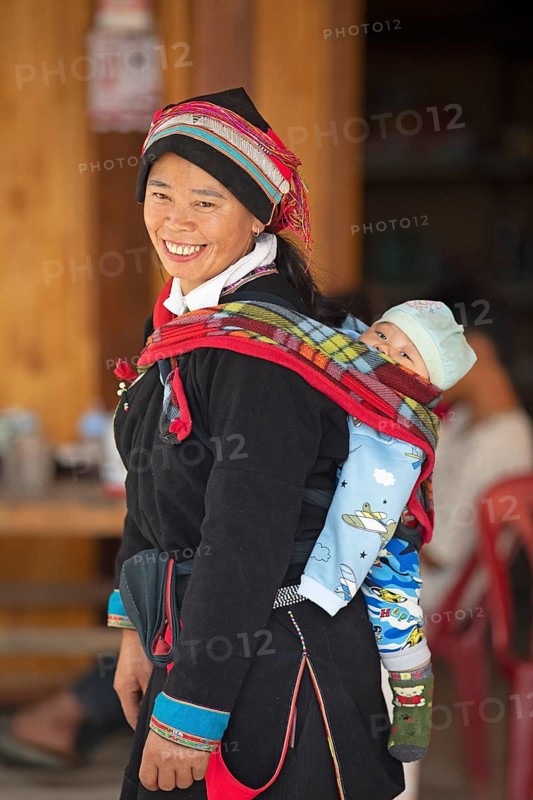 Vietnamese woman, 43 years old, in traditional traditional costume of the Dao minority, carrying her son, 3 months, on her back, Nam Dam Dao Cultural Village, Ha Giang province, Vietnam, Asia