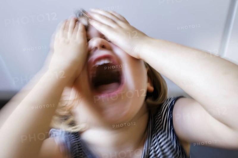 Symbolic photo on the subject of tantrums in children (staged scene) . A little girl holds her hands in front of her eyes and screams with her mouth open. Berlin, 21.08.2024