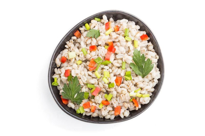 Pearl barley porridge with vegetables in blue ceramic bowl isolated on white background. Top view, flat lay, close up. Russian traditional cuisine