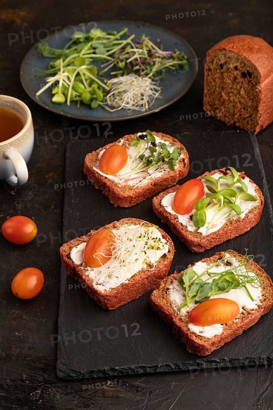 Red beet bread sandwiches with cream cheese, tomatoes and microgreen on black concrete background. Side view, close up