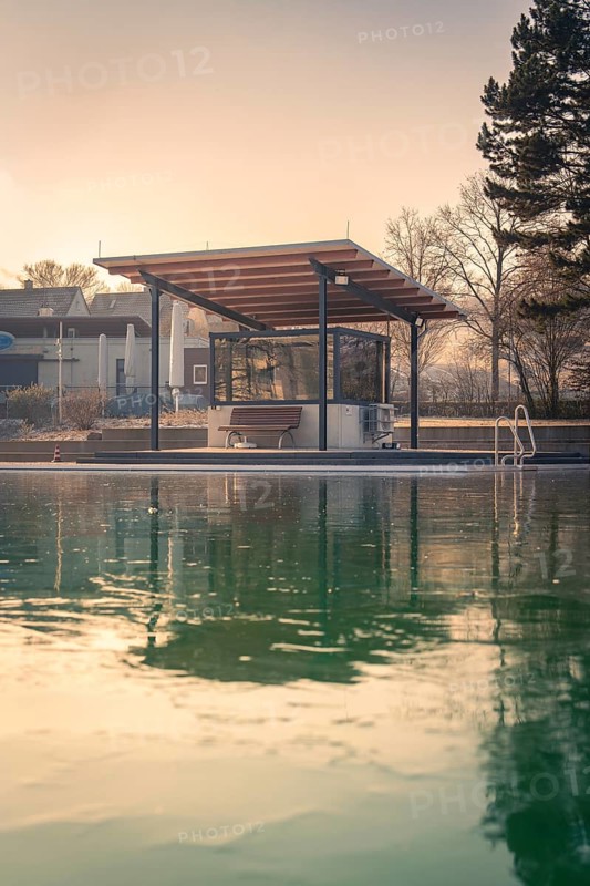 Outdoor pool with modern roofing at the edge of the pool, reflection of the sunset in the frozen water, ENCW outdoor pool Calw, Stammheim, Black Forest, Germany, Europe