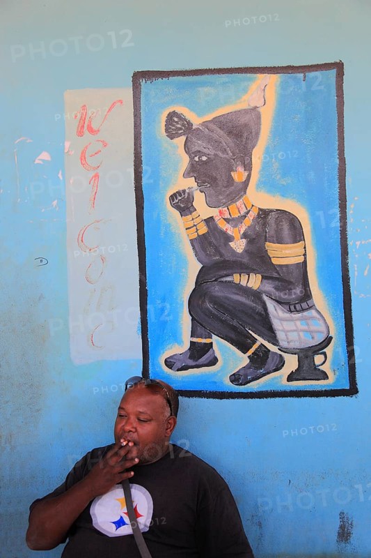 South Ethiopia, in Dimeka, local man sitting in front of a painting in a cafe and smoking a cigarette, Ethiopia, Africa