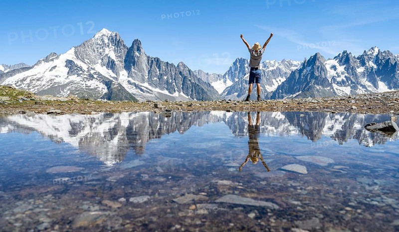 Mountaineer triumphantly raising his arms in the air, in front of a mountain landscape, reflection in a small mountain lake, mountain peaks Aiguille Verte and Grandes Jorasses, mountain panorama with Mont Blanc massif, Aiguille Rouge, Chamonix-Mont-Blanc, Haute-Savoie, France, Europe