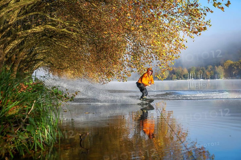 Essen, North Rhine-Westphalia, Germany, Golden autumn on Lake Baldeney. Wakeboarder in the morning mist on the lakeside path under plane trees gliding over the water using a mobile tow lift, mobile Sculpture Winch, Europe