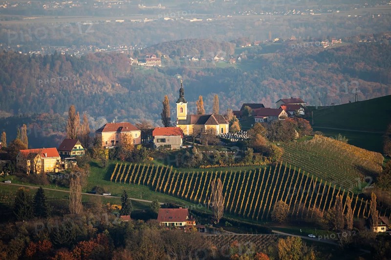 Autumn atmosphere in the evening light, forest with foliage colouring, hilly landscape, vineyards, church of Kitzeck, view from the Demmerkogel lookout point, St. Andrä-Höch, Sausal wine country, Styria, Austria, Europe
